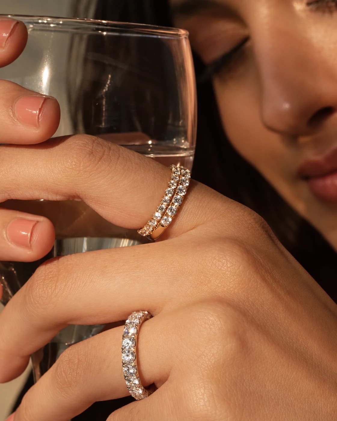 Yellow and white gold diamond eternity bands worn on a hand holding a glass