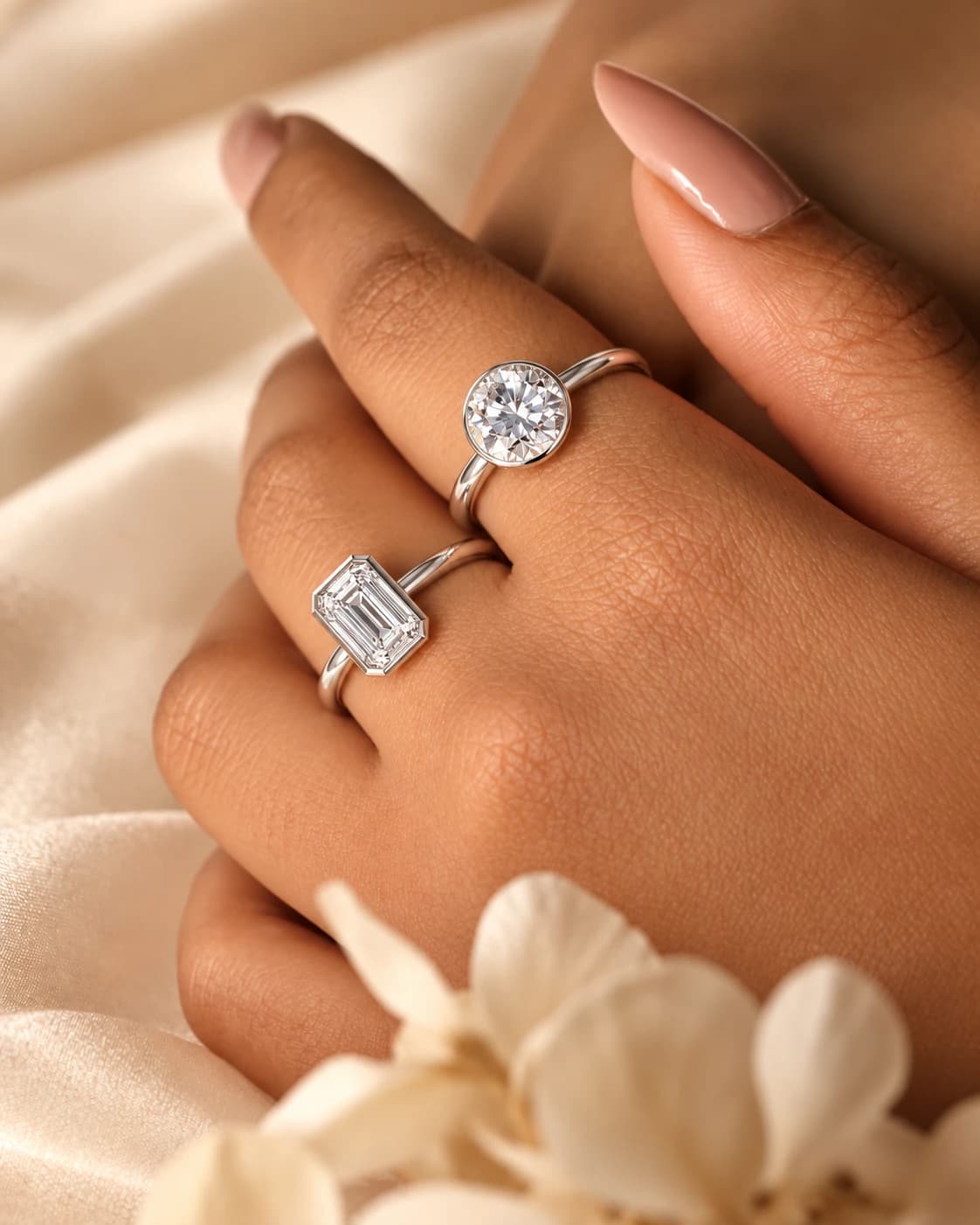 Round and emerald-cut bezel-set diamond rings in white gold, worn on one hand